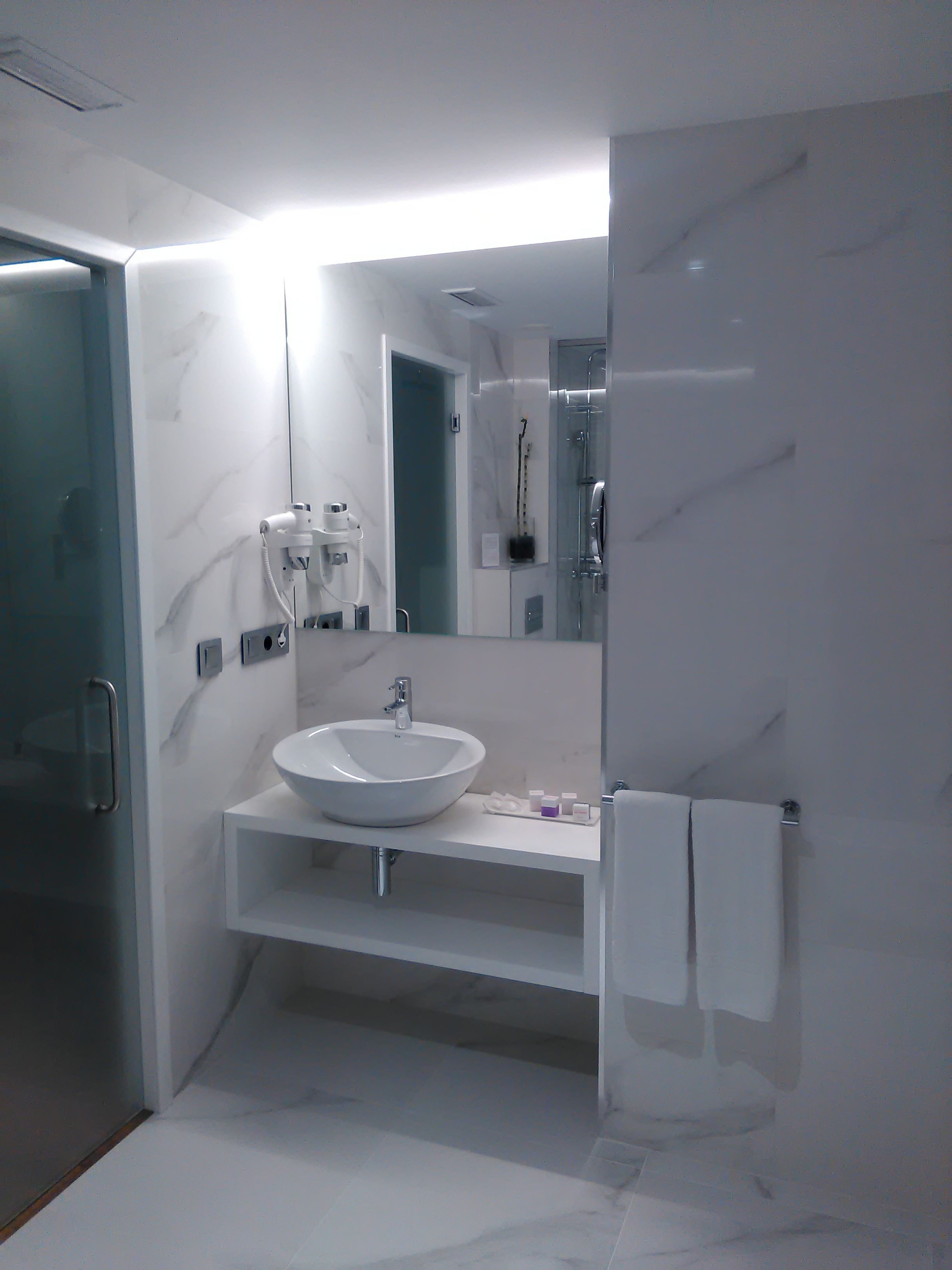 A modern bathroom with a white marble sink, a glass shower enclosure, and a large mirror.