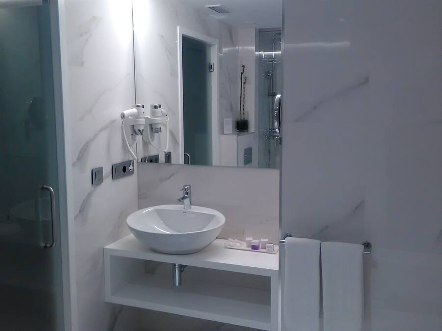 A modern bathroom with a white marble sink, a glass shower enclosure, and a large mirror.