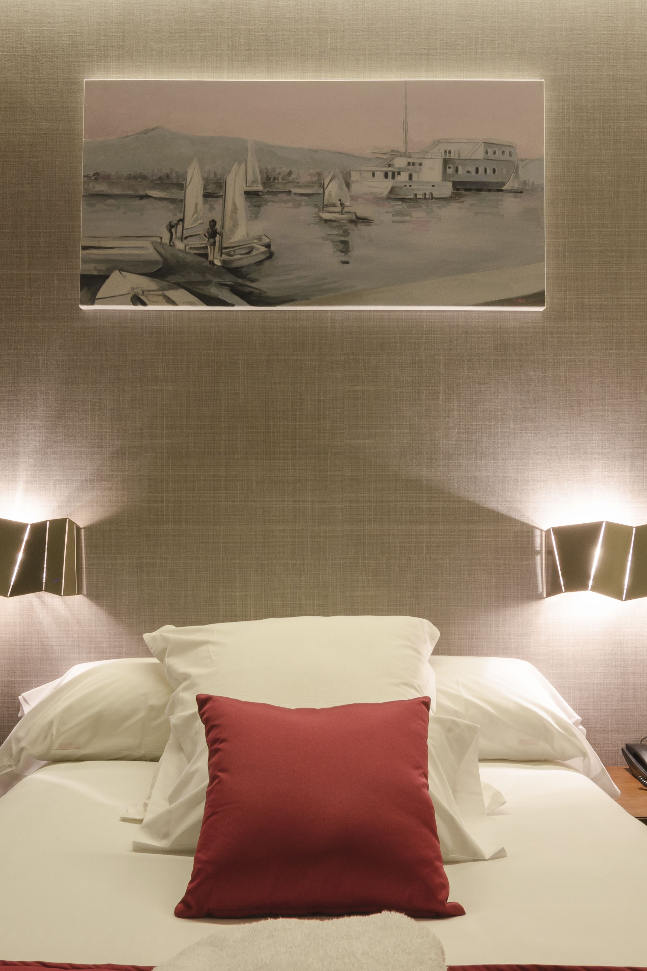 Una habitación de hotel con una cama, un cuadro de una escena portuaria y dos lámparas de noche.