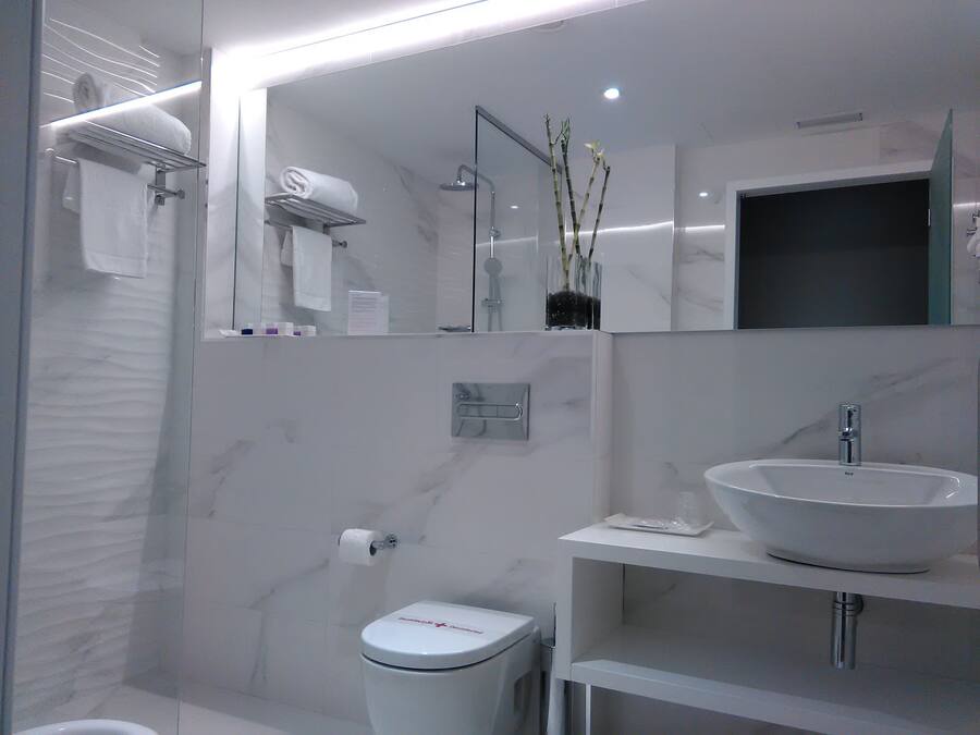 Ein modernes Badezimmer mit Duschkabine aus Glas, Toilette in Weiß, Waschbecken mit Spiegel darüber und Handtuchhalter.