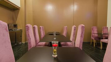 Une salle de conférence avec une longue table, des chaises roses et un verre d’eau posé sur la table.