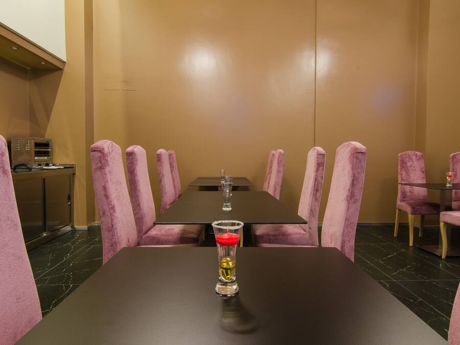 Un salón de conferencias con una larga mesa, sillas rosadas y un vaso de agua sobre la mesa.