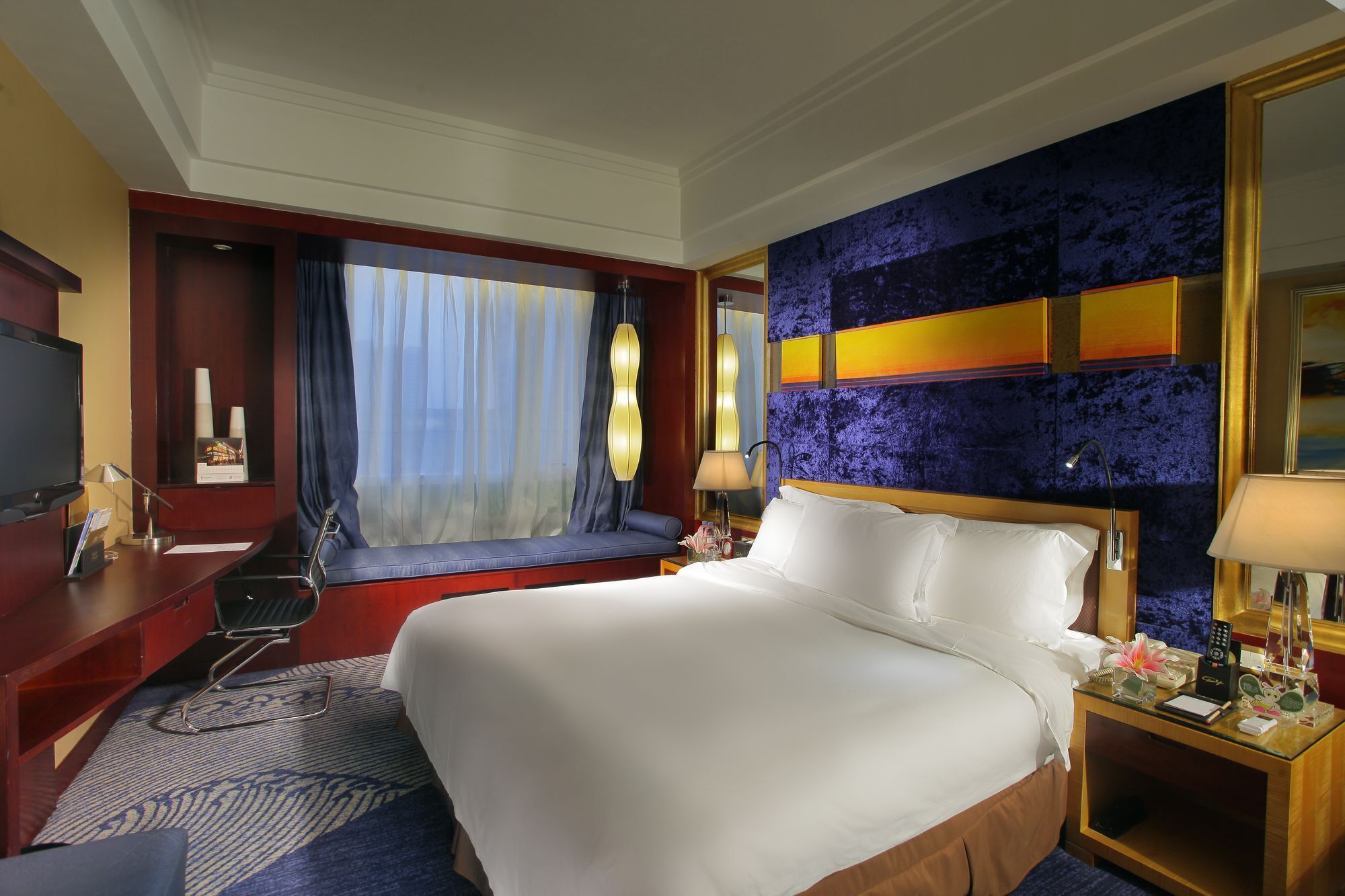 Ein Hotelzimmer mit einem großen Bett, einem Schreibtisch, einem Fernseher und einem Fenster mit Vorhängen.