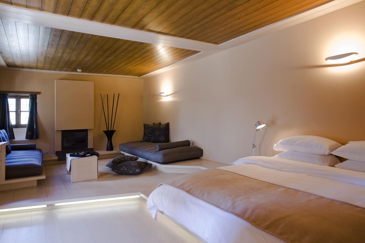 Un dormitorio moderno con techo de madera, un sofá, una cama y una mesita.