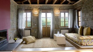 A cozy room with stone walls, a wooden ceiling, a sofa, a coffee table, and a fireplace. - Kipi Suites (Zagori)