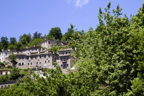 A hillside village with stone buildings, lush greenery, and a clear blue sky.