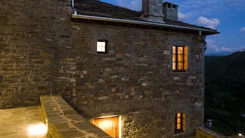 A stone building with a stone staircase leading to a door, set against a mountainous backdrop.