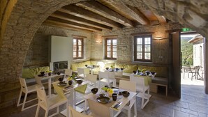 A rustic dining area with stone walls, wooden beams, and white furniture. Tables are set with bowls, plates, and cutlery. - Kipi Suites (Zagori)