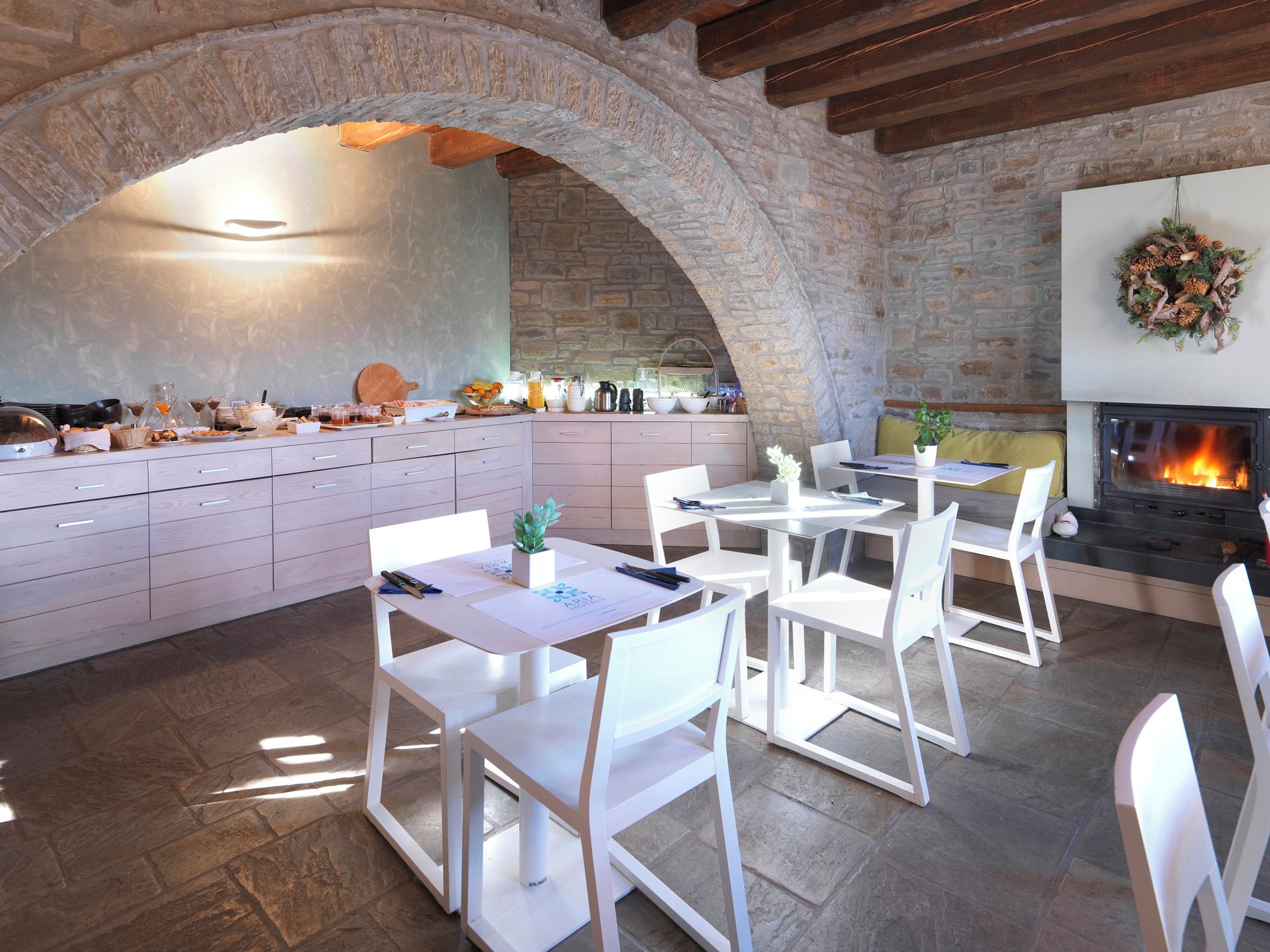 A rustic kitchen with stone walls, a fireplace, and a dining area with white chairs and tables.