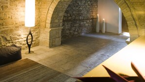 A stone-walled room with a wooden ceiling, a table with candles, and a bench. - Kipi Suites (Zagori)