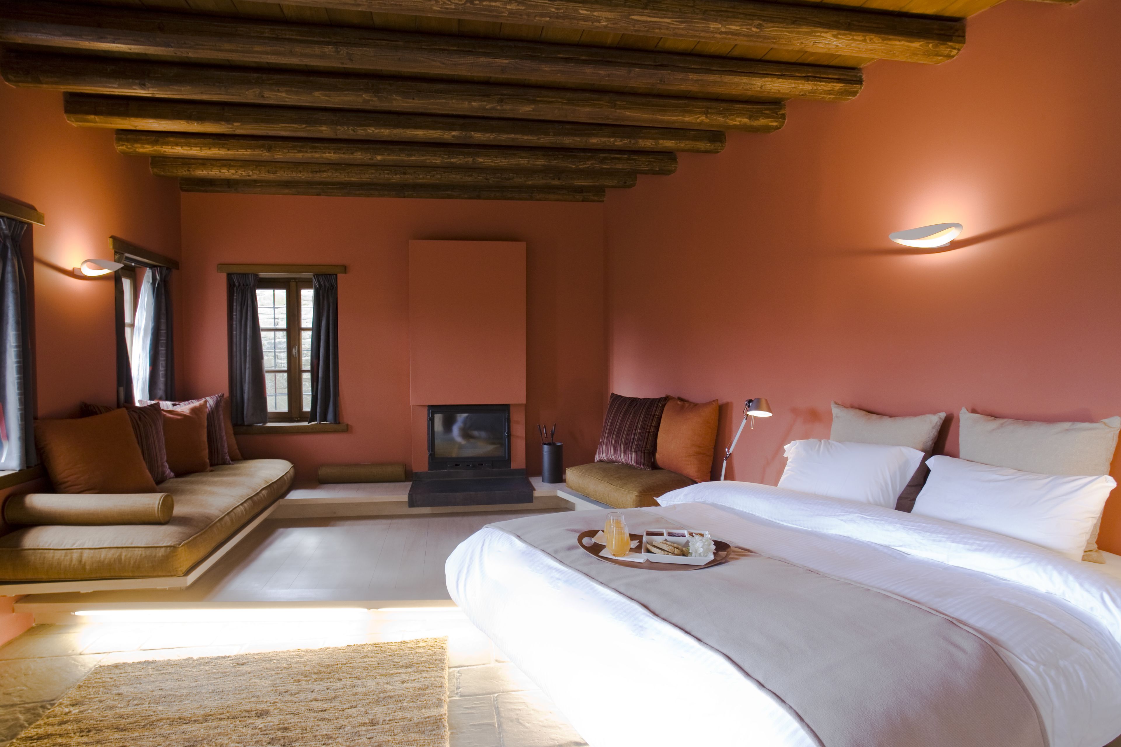 A bedroom with a large bed, a sofa, a fireplace, and a tray with breakfast items.