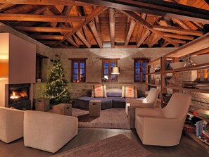 A cozy living room with a fireplace, a Christmas tree, and a stone wall. - Kipi Suites (Zagori)
