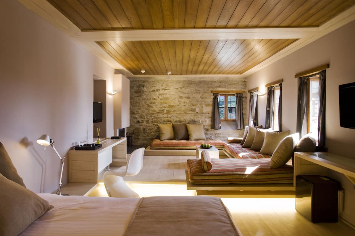Un dormitorio moderno con pared de piedra, techo de madera y una cama grande con muchas almohadas.