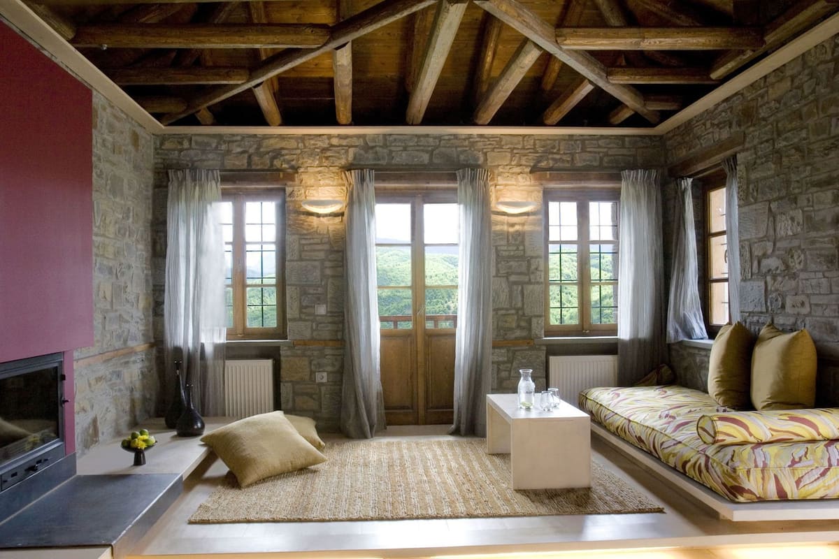 Una habitación rústica con paredes de piedra, techo de madera, un sofá, una mesita de centro y una chimenea.