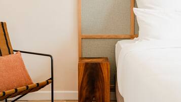 A bedroom with a bed, a nightstand, a lamp, a chair, and a small wooden stool.