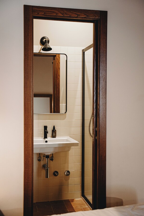 A bathroom with a wooden-framed mirror, a white sink, and a shower door. - Aethos Hotel Saragano (Gualdo Cattaneo)
