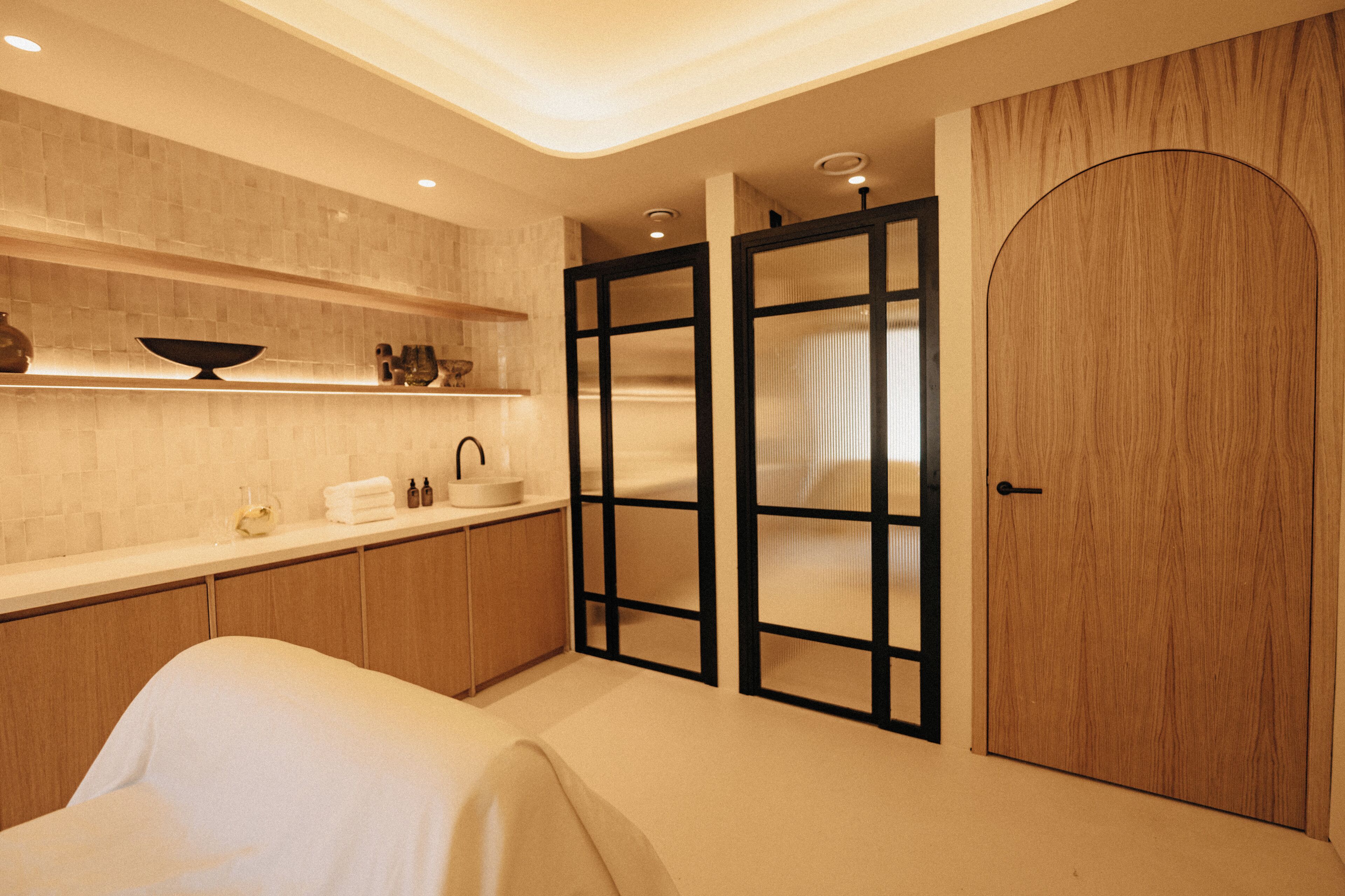 A modern bathroom with a large mirror, wooden cabinets, and a white sink.