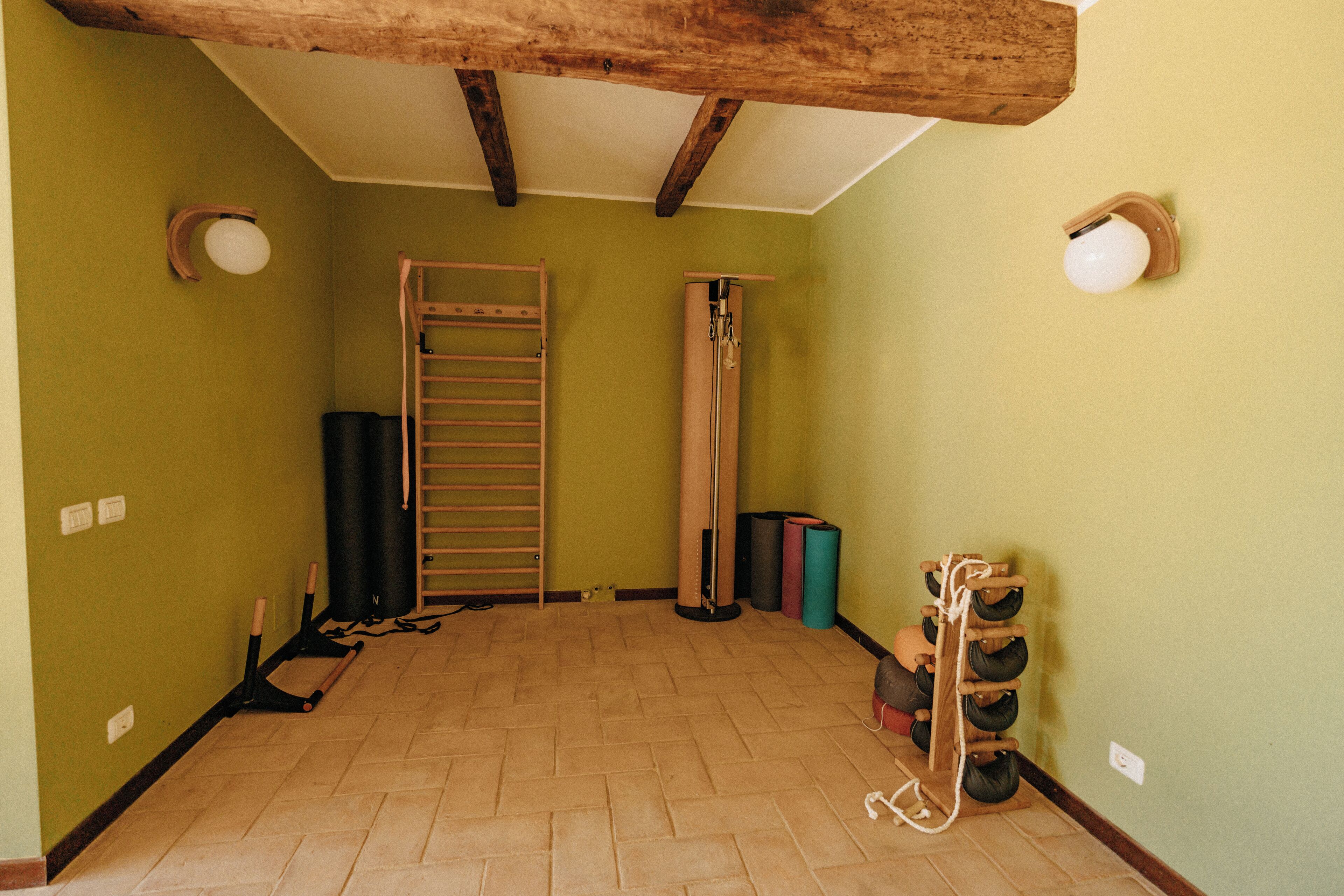 Een kamer met een houten plafond, een ladder, een optrekstang en een schoenenrek aan de muur.