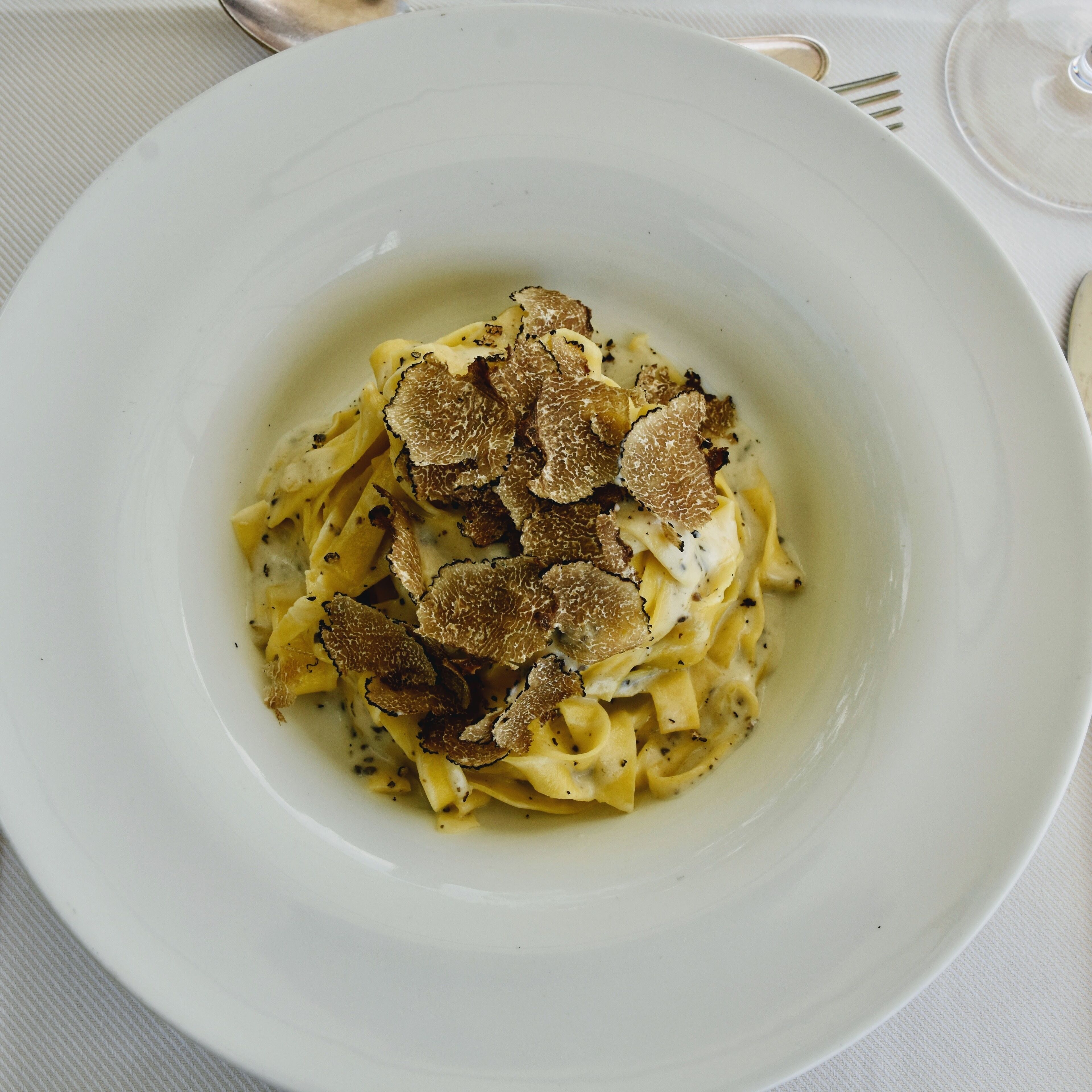 A white plate with fettuccine pasta topped with shaved truffles.