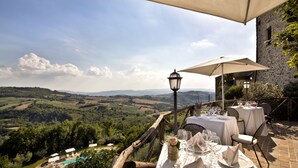 Une table dressée pour le dîner, avec vue sur des collines verdoyantes et une piscine en arrière-plan.