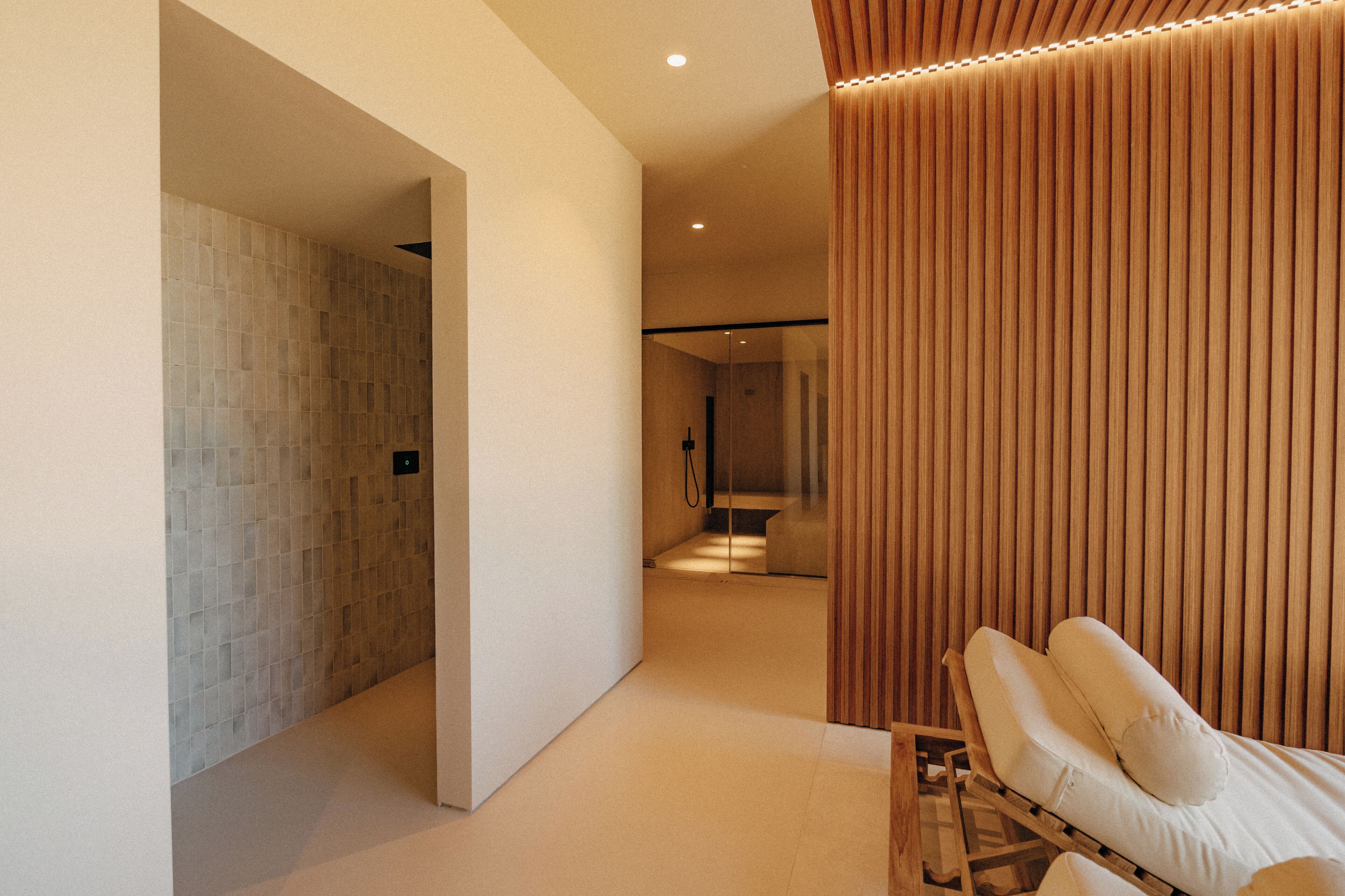 A modern spa room with a massage table, a wooden panel wall, and a tiled shower area.