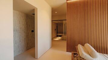 A modern spa room with a massage table, a wooden panel wall, and a tiled shower area.