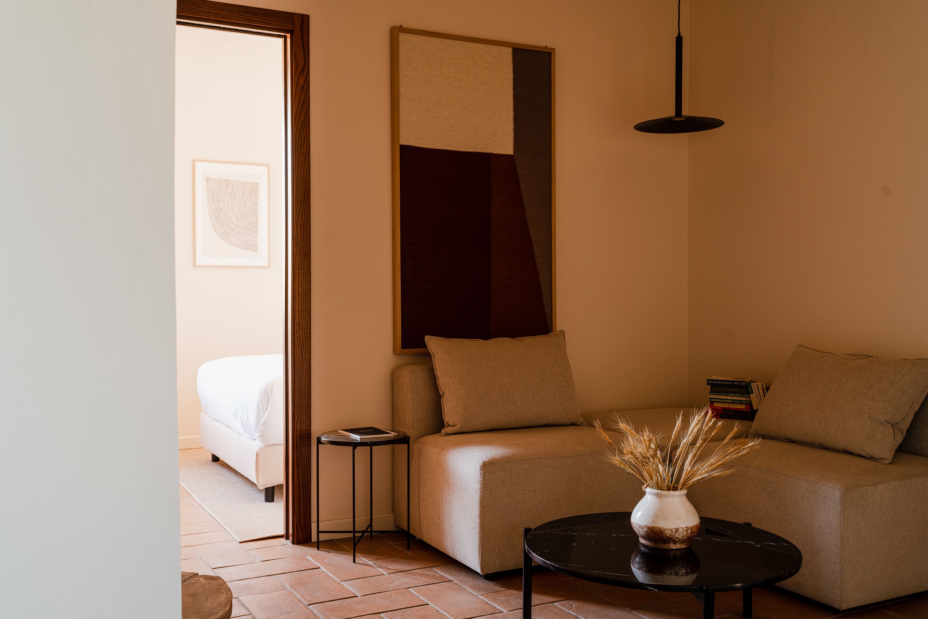 Uma sala de estar moderna com um sofá, uma mesinha lateral, um vaso com plantas secas e um lustre.