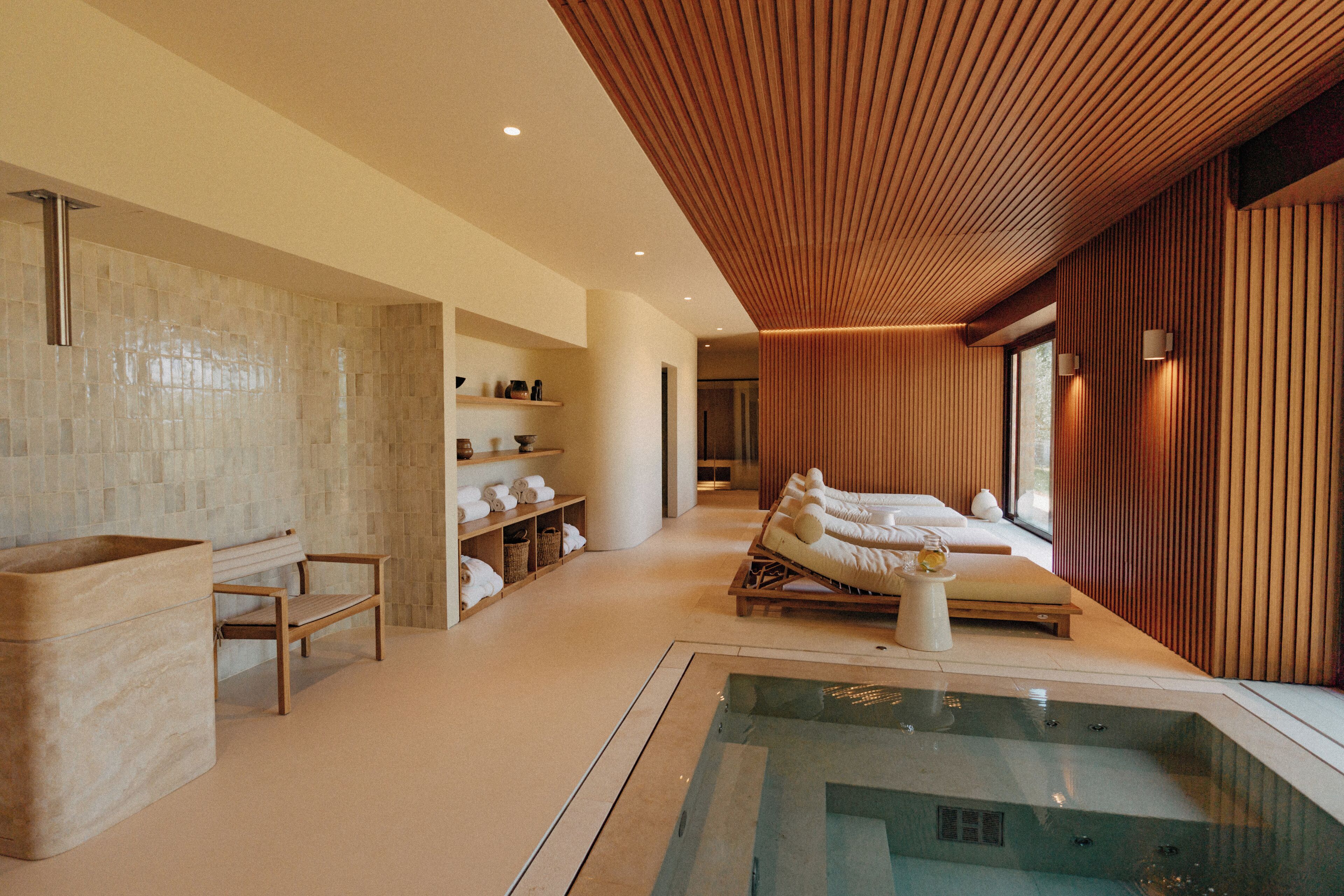 A modern spa room with a glass-enclosed hot tub, wooden furniture, and a large window providing natural light.