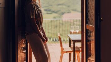 A woman standing at a glass door with a view of a balcony and outdoor furniture.