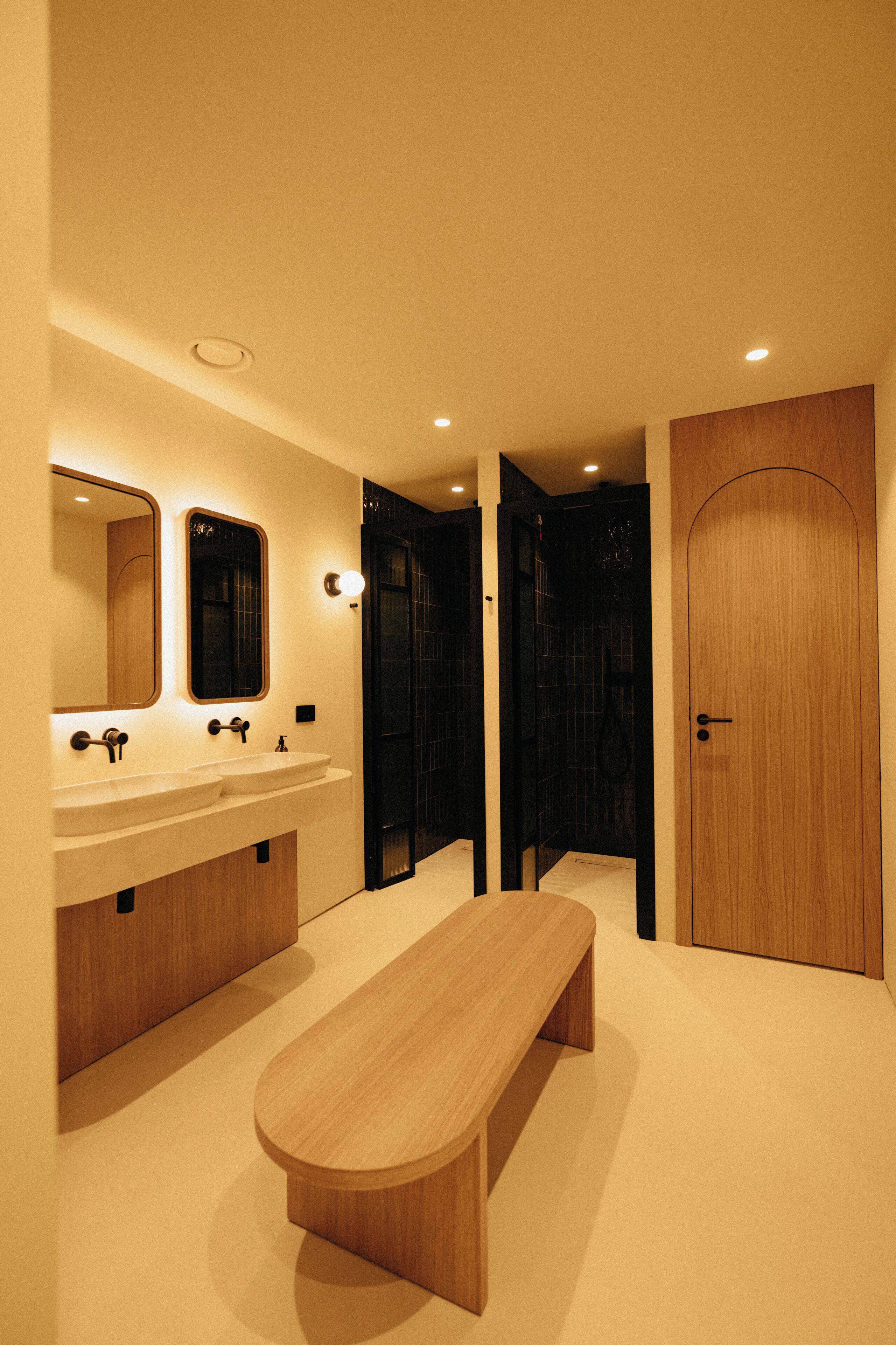 Une salle de bain moderne avec deux lavabos, un banc et une porte en bois.