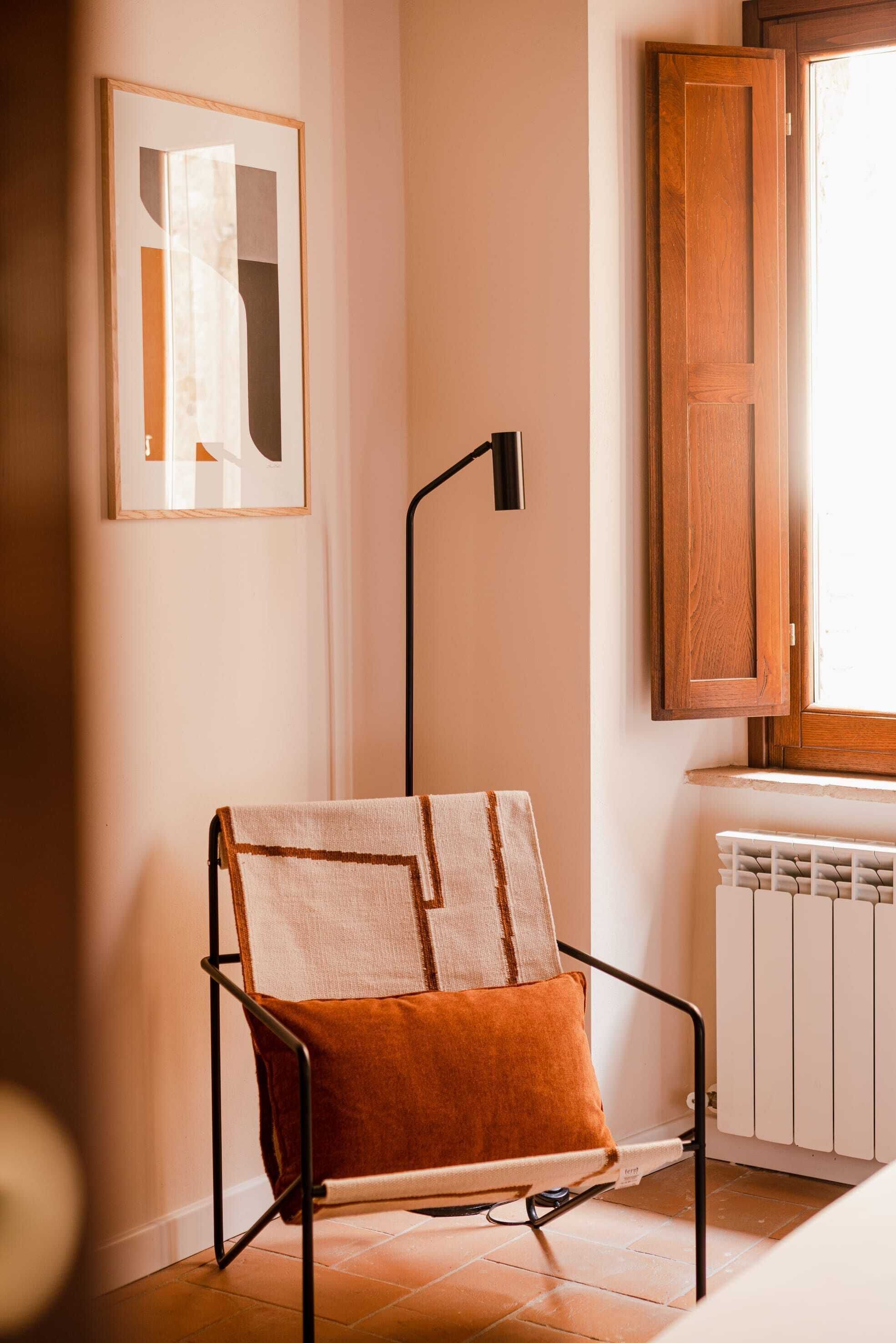 A chair with a cushion, a floor lamp, a radiator, and a window with a wooden shutter.