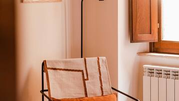 A chair with a cushion, a floor lamp, a radiator, and a window with a wooden shutter.