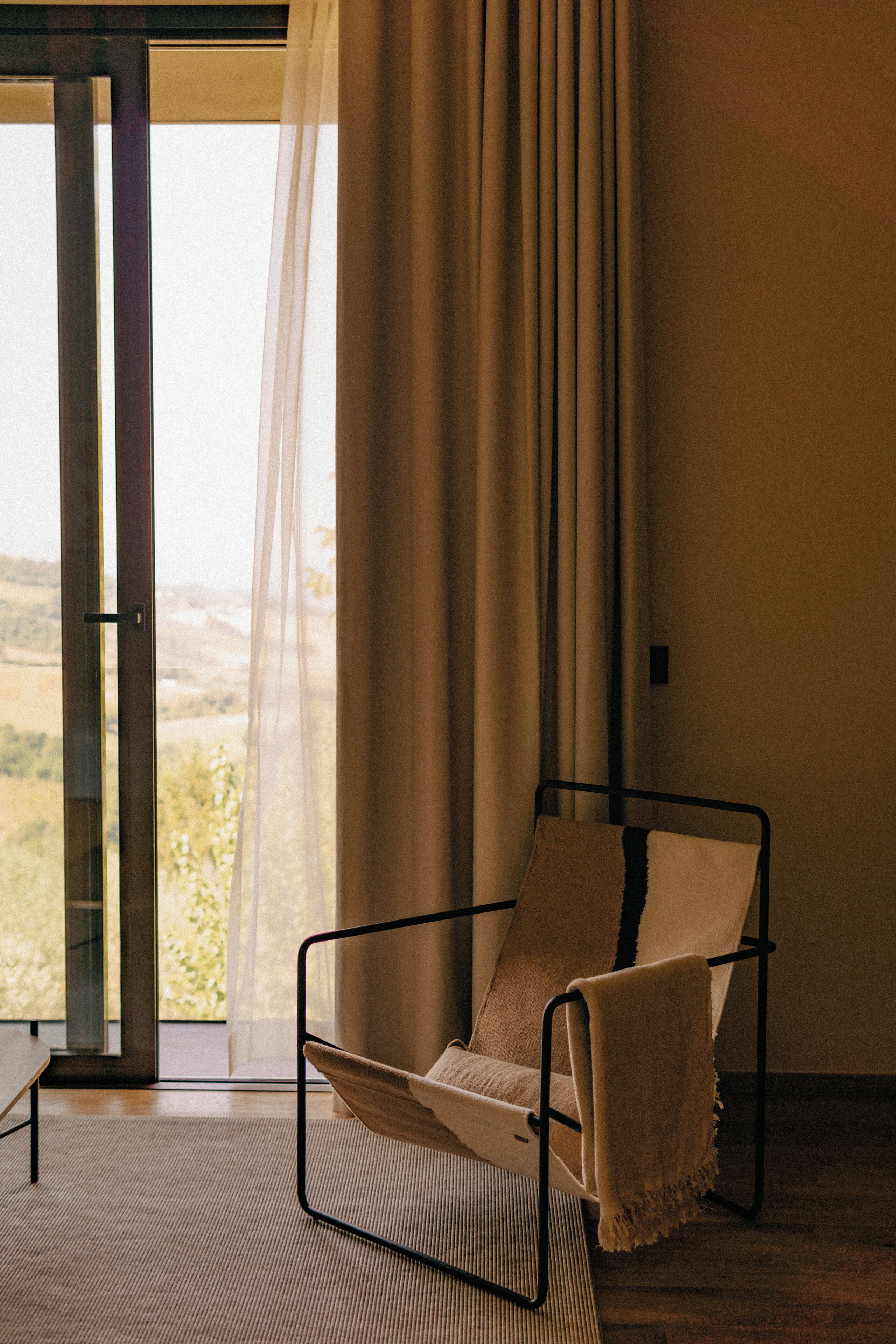 A room with a large window, a chair with a cushion, and a view of a landscape.