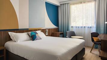 Una habitación de hotel con una cama grande, un escritorio, una silla y un ventanal con cortinas.