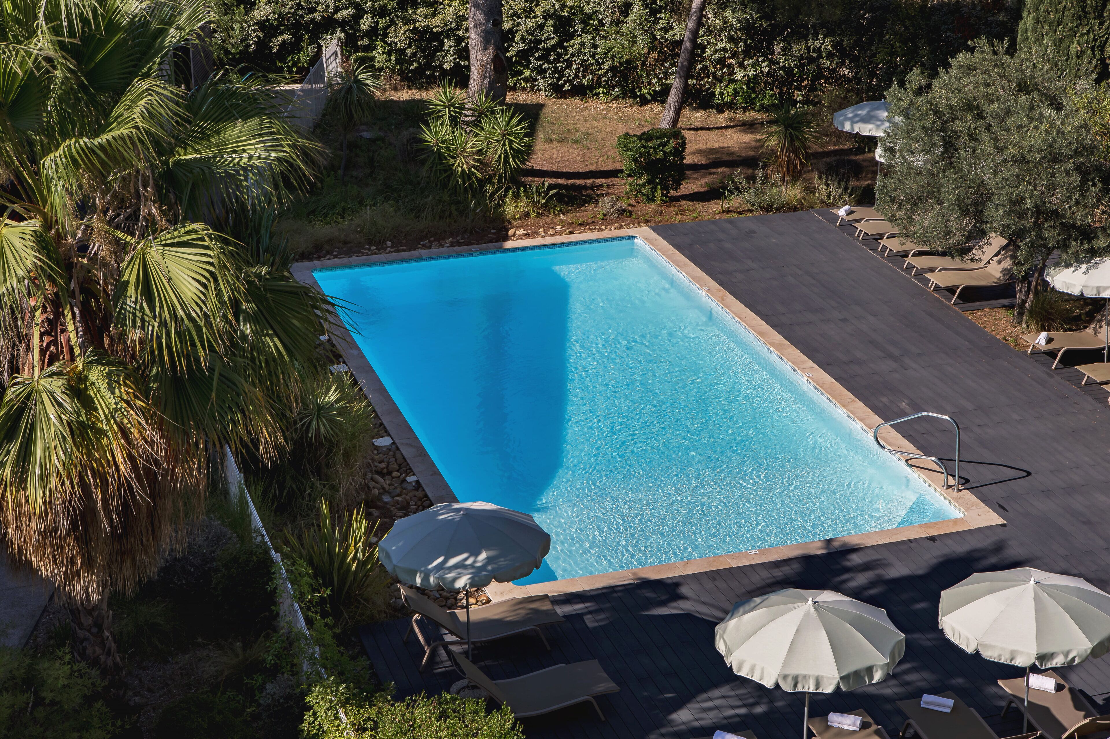 A rectangular swimming pool with a tiled edge, surrounded by a deck area with lounge chairs and umbrellas.