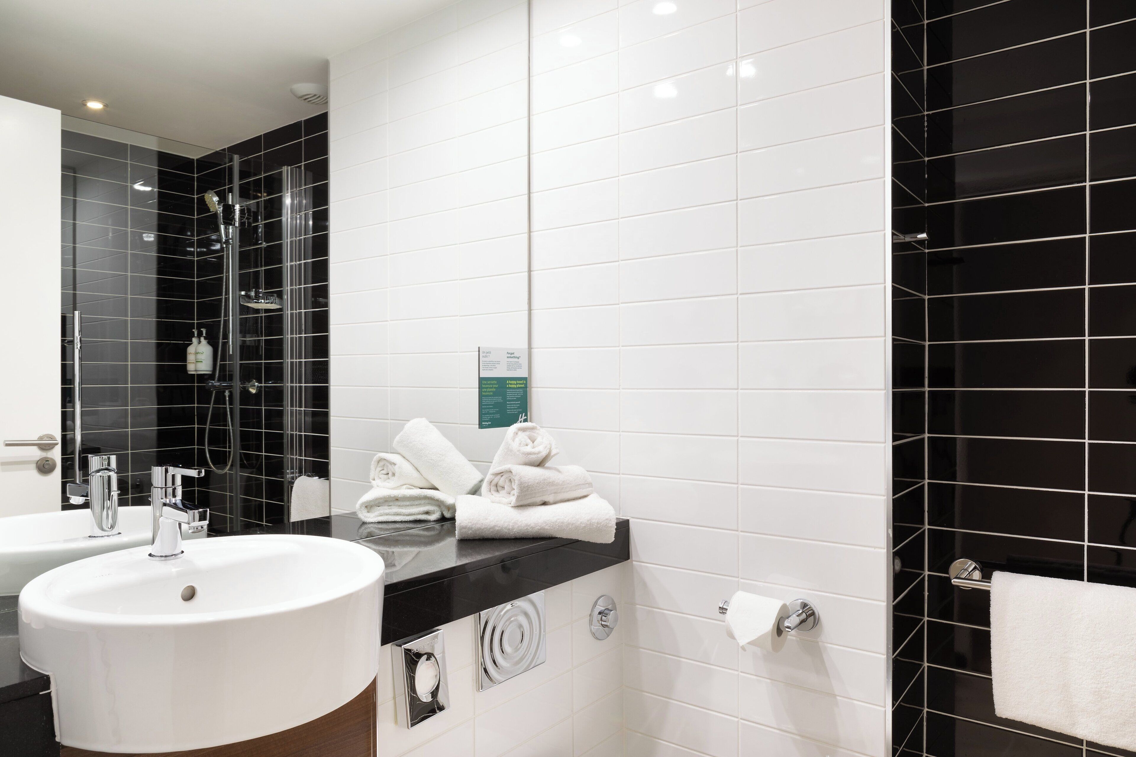 Une salle de bain moderne avec un lavabo blanc, une baignoire noire et une cabine de douche en verre.