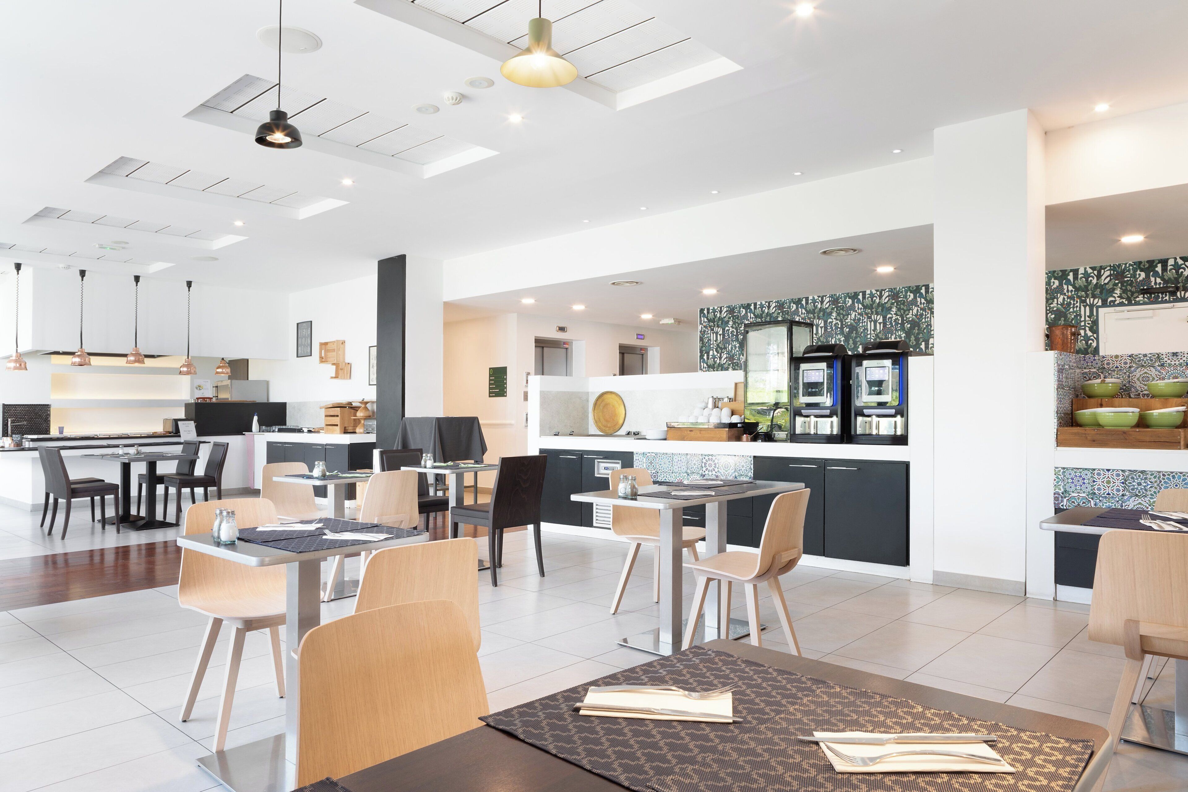 A modern hotel lobby with a dining area, kitchen, and a reception desk.