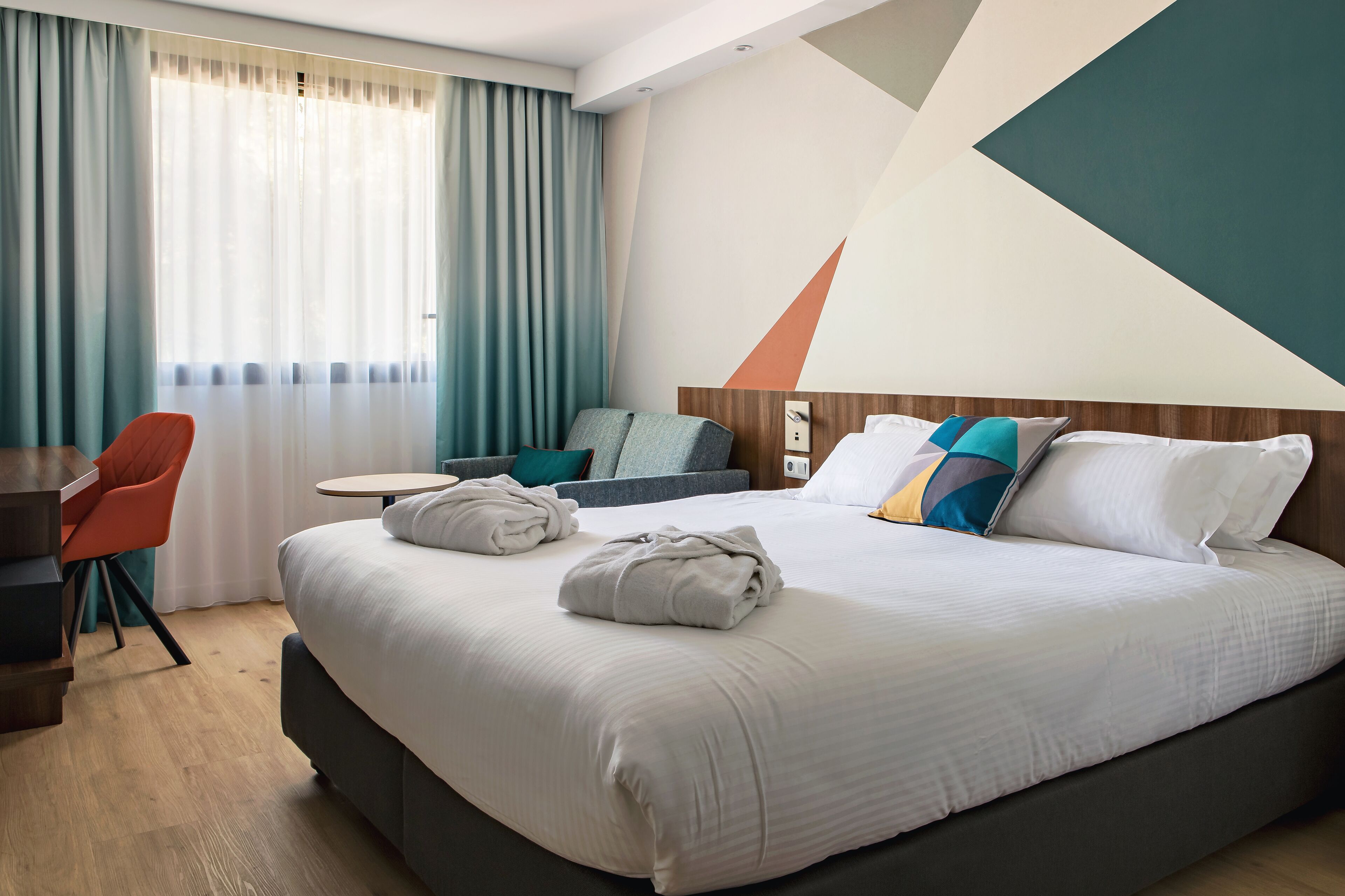 A hotel room with a large bed, a desk, a chair, and a small table.