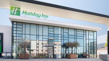 Un hotel Holiday Inn con fachada de vidrio moderna, una banca de madera en el exterior y cielo despejado.