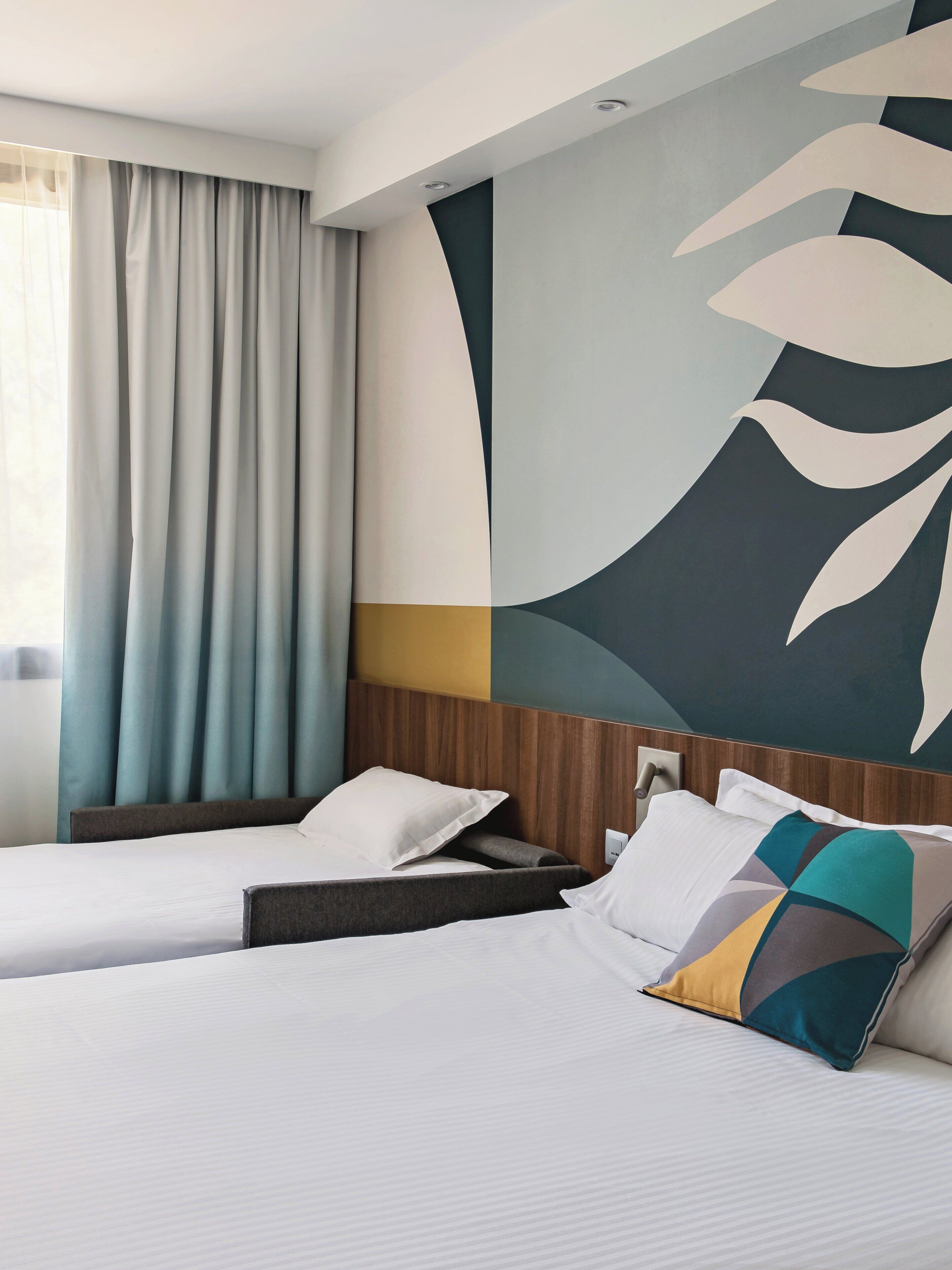 A hotel room with two beds, a large abstract wall art, and a window with curtains.