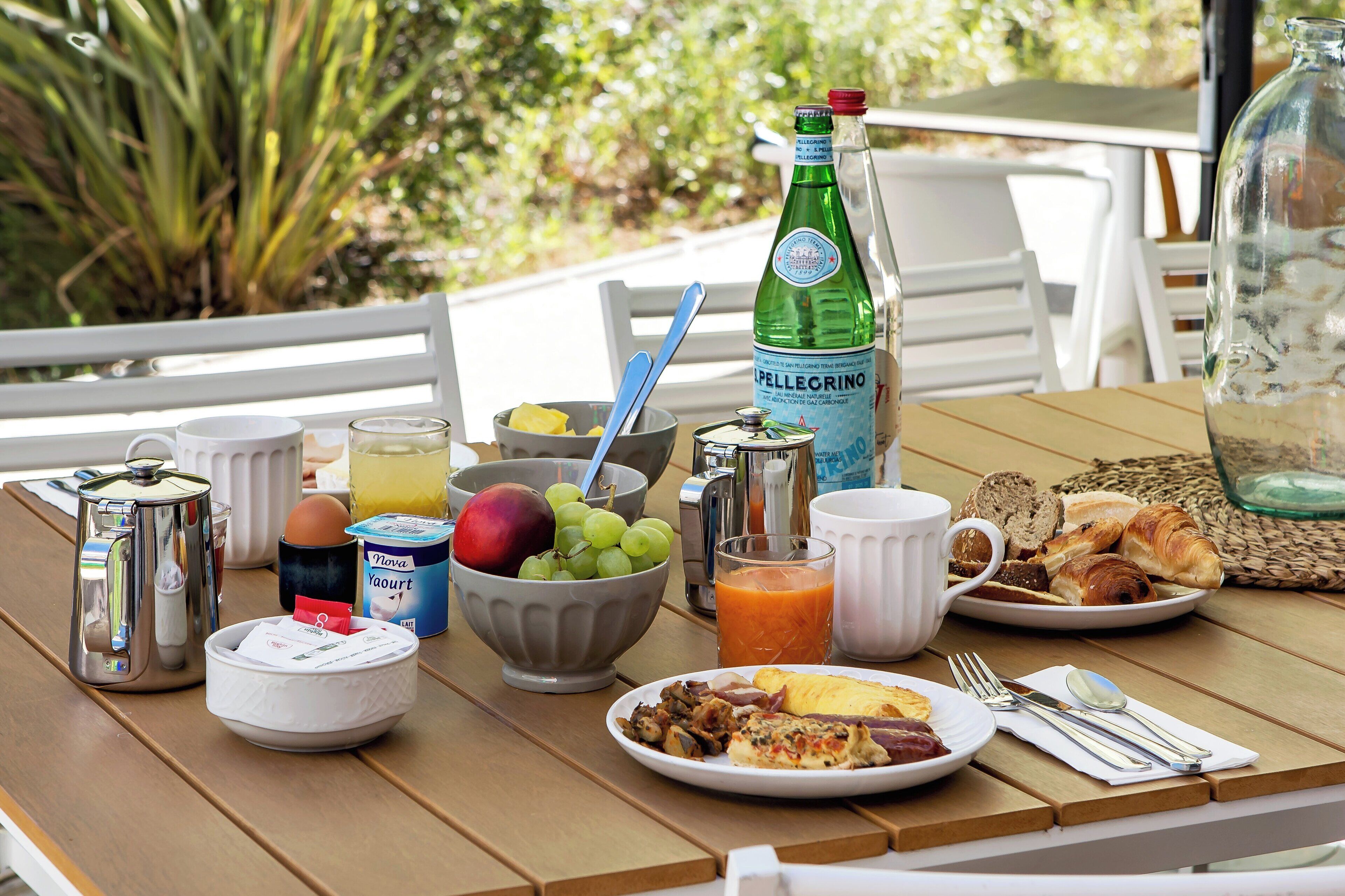 A breakfast table with a variety of food items, including fruits, bread, and a bottle of Pellegrino water.