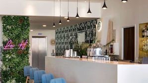 A modern bar area with a bar counter, blue bar stools, hanging pendant lights, and a green wall with a neon sign. - Holiday Inn Marseille Airport by IHG (Vitrolles)