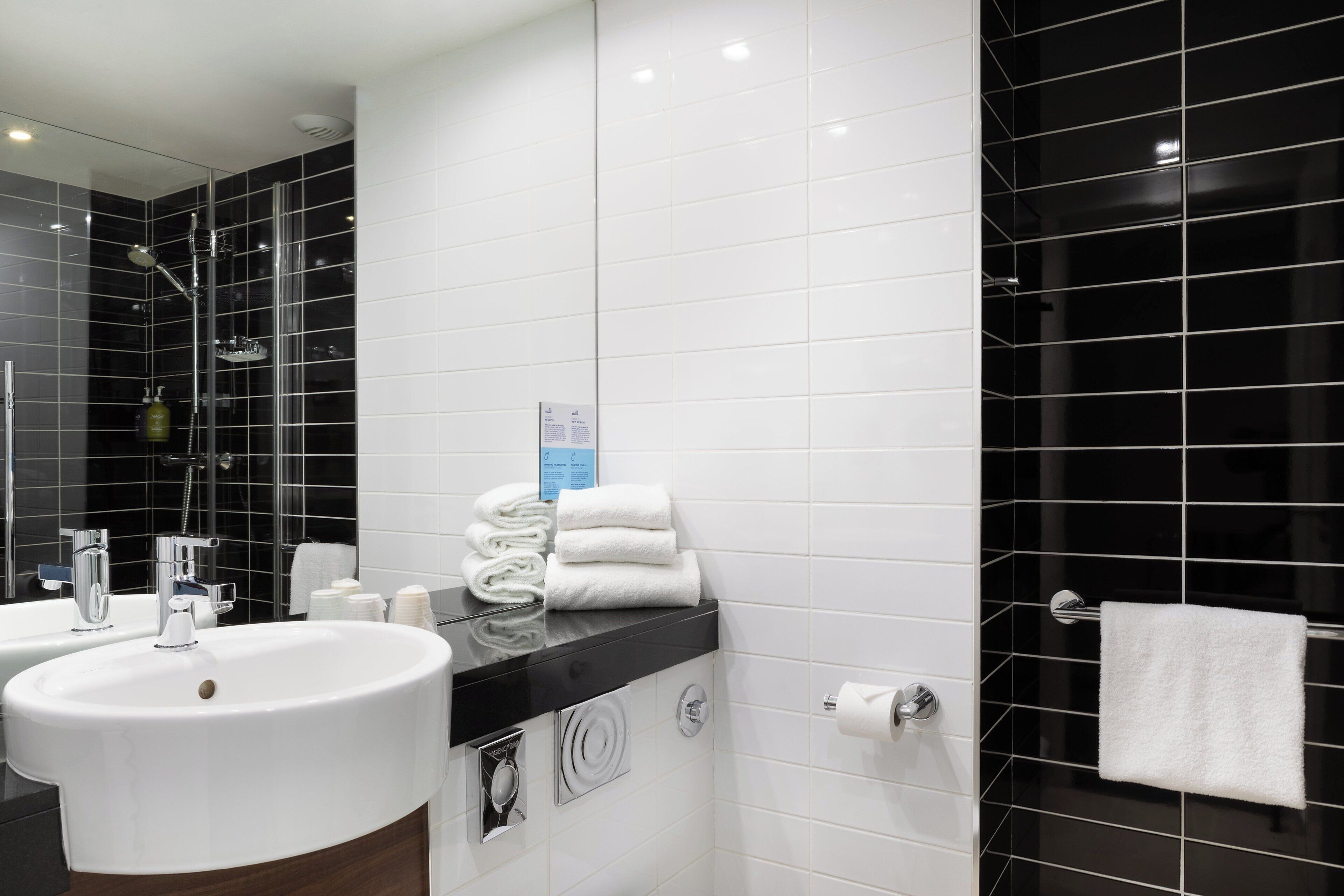 A modern bathroom with a white sink, a glass shower enclosure, and black tiled walls.