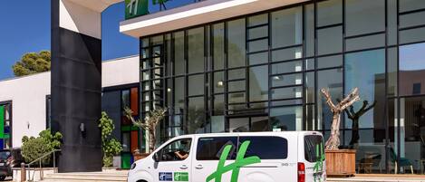 A white van with green branding parked in front of a Holiday Inn hotel.