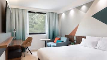 A modern hotel room with a large bed, a desk, a chair, and a small table.