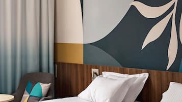 Une chambre d’hôtel avec deux lits, une tête de lit en bois, un mur décoré d’œuvres d’art abstraites, une chaise et une table.