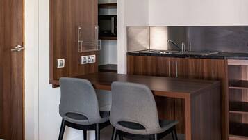 Una cocina compacta con cubierta de madera, dos sillas grises y un lavamanos de acero inoxidable.