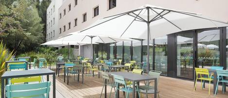 An outdoor seating area with tables and chairs, umbrellas, and a building in the background.