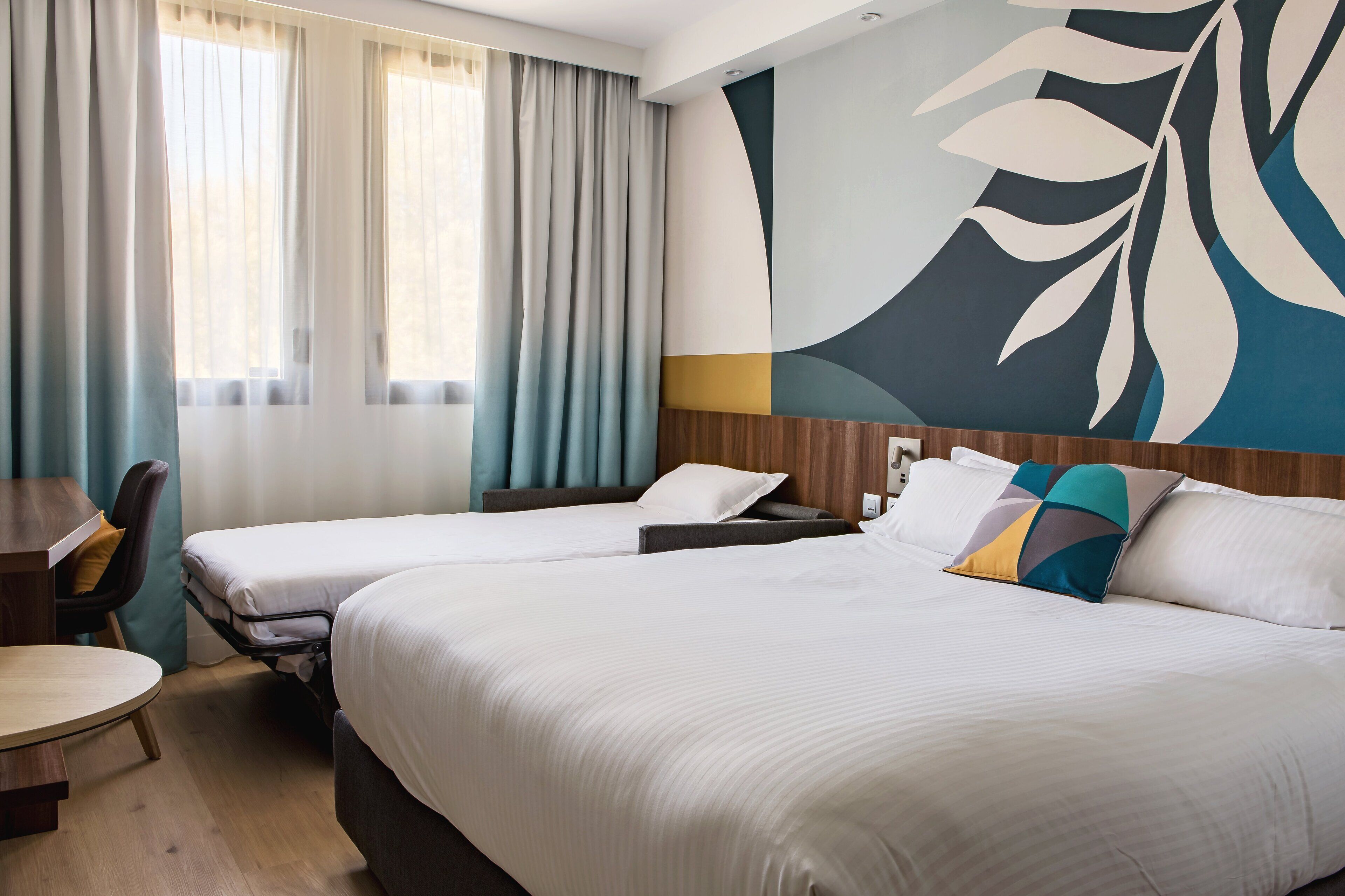 A hotel room with two beds, a desk, and a large abstract wall mural.
