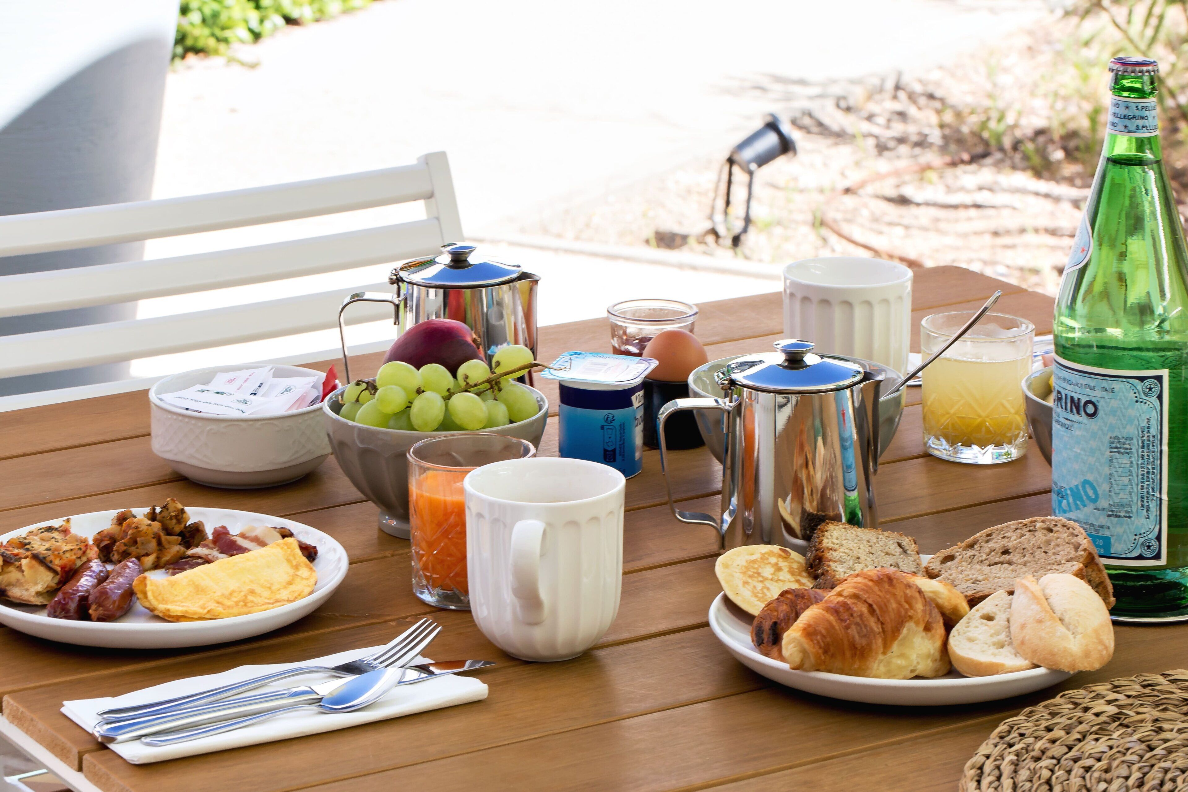A breakfast table with plates of food, a coffee pot, a bottle of water, and a glass of orange juice.
